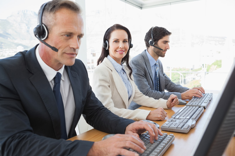 two men and a woman wearing suits and headsets sitting at computers